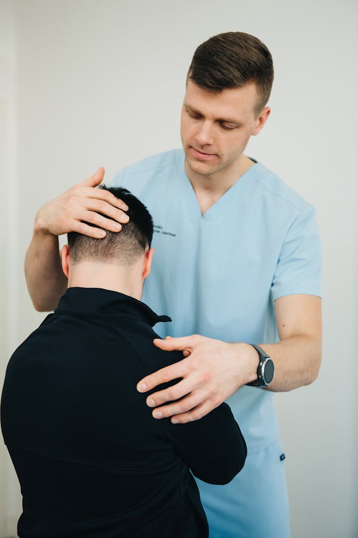 A physiotherapist examines a male patient's neck for pain relief in a clinic setting.