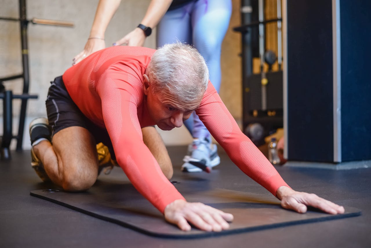 Senior man engaging in assisted stretching exercises for healthy living in a gym.